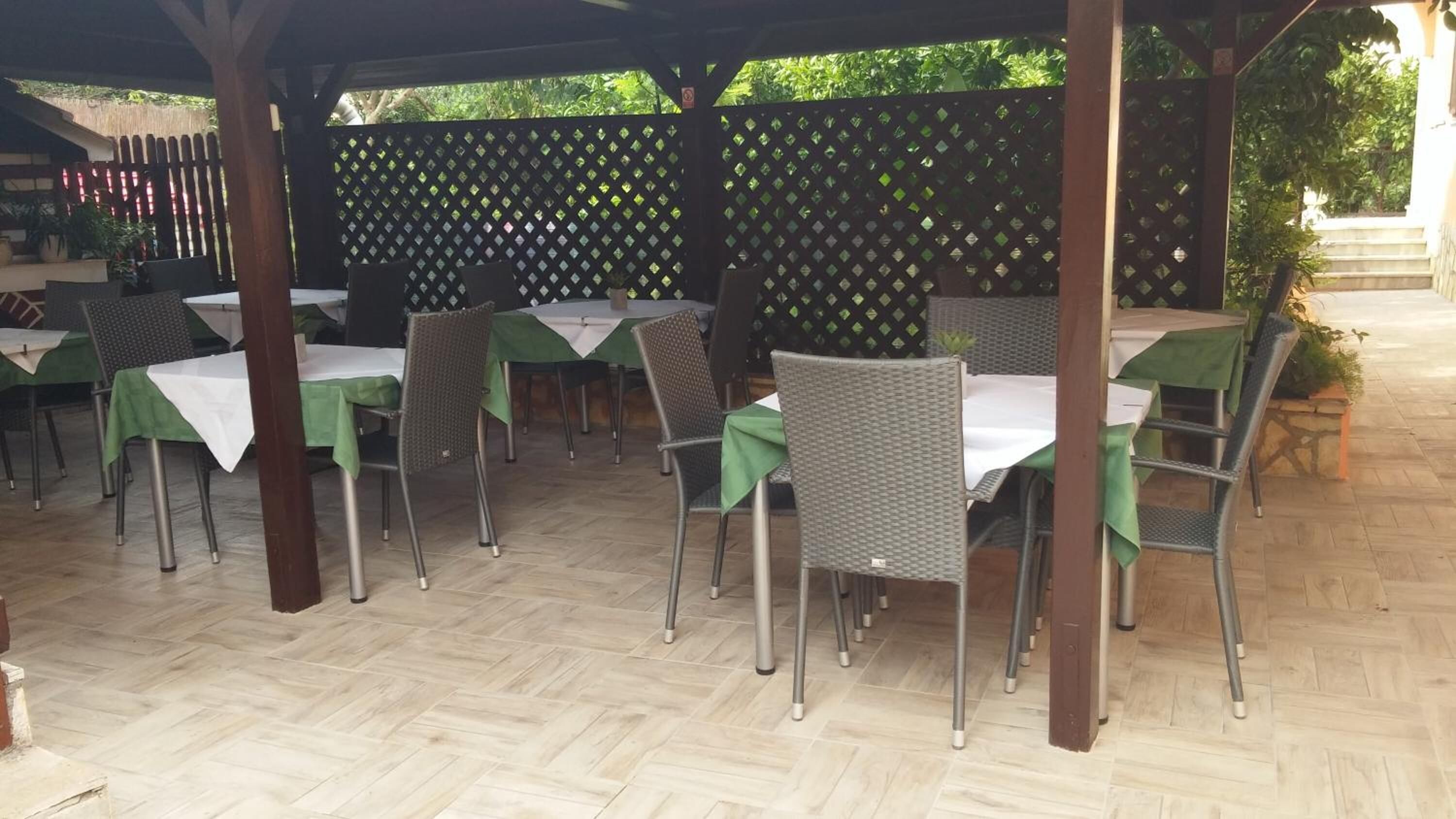 Un patio al aire libre con mesas y sillas, cubierto por una pérgola de madera.