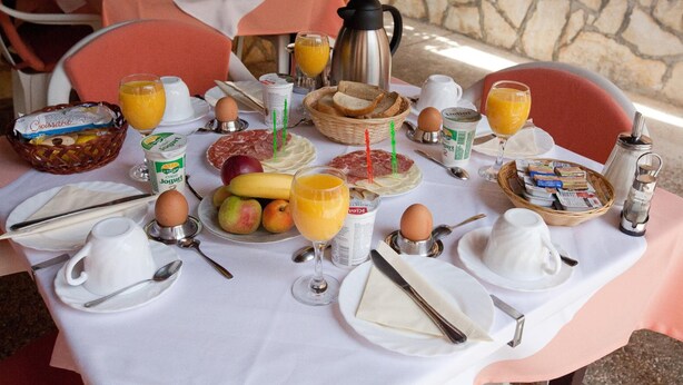 Una mesa de desayuno servida con diversos alimentos, como pan, huevos y fruta, además de bebidas y salsas.