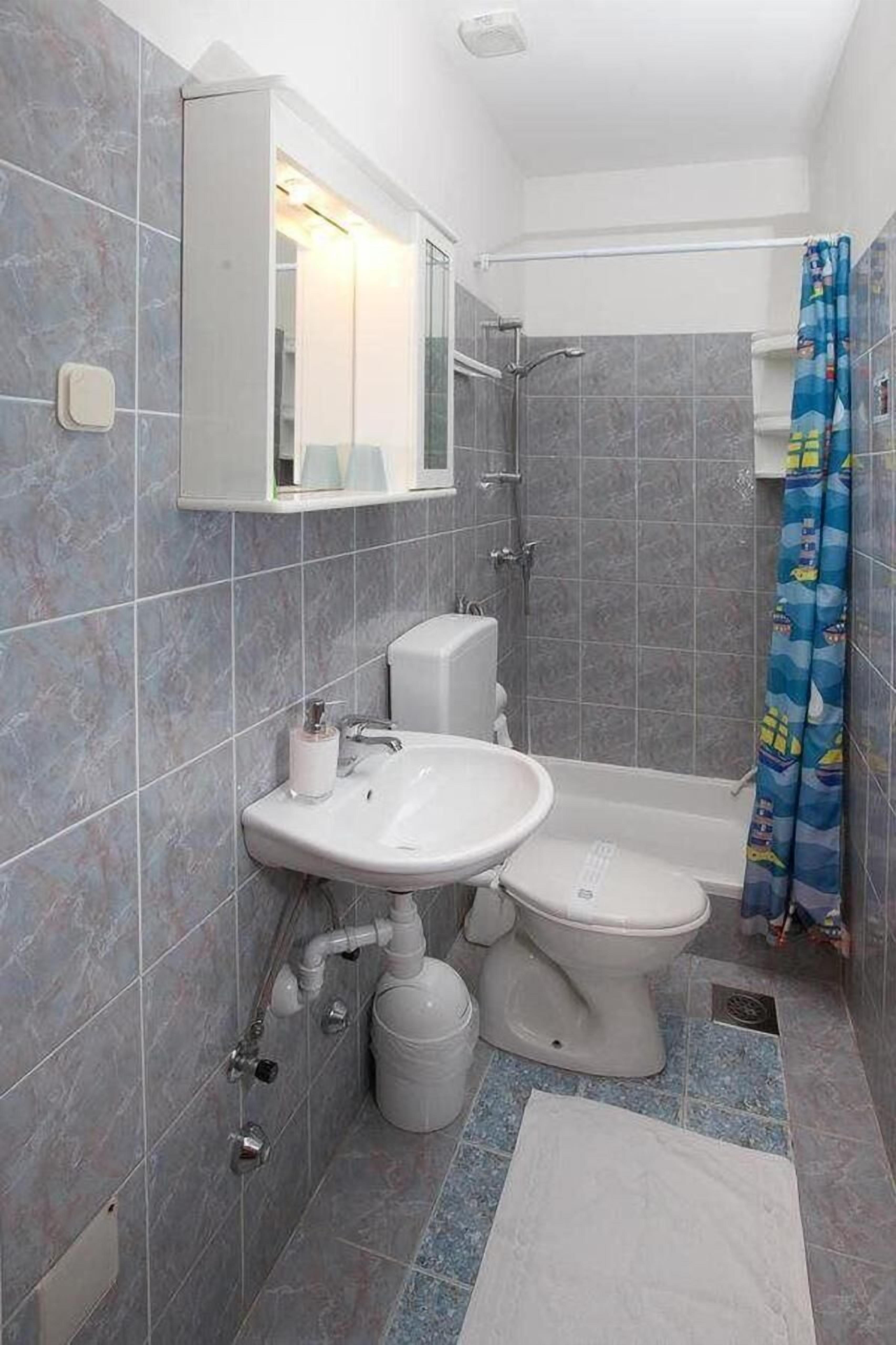 A bathroom with grey tiles, a white sink, a toilet, and a shower area.
