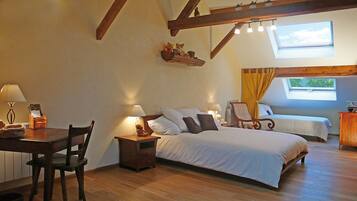 Une chambre confortable avec un grand lit, un plus petit lit, un bureau avec une chaise et une table de chevet avec une lampe. Il y a une fenêtre donnant sur les arbres et un puits de lumière au-dessus du lit.