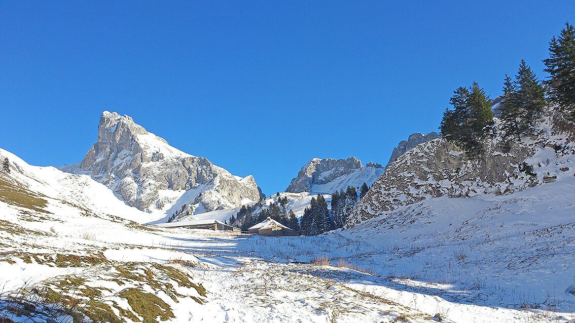 A mountainous landscape with snow-covered peaks and a clear blue sky.