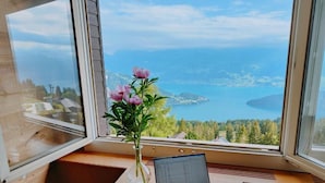 Una computadora portátil sobre un escritorio de madera junto a una ventana con vista a un cuerpo de agua y vegetación.