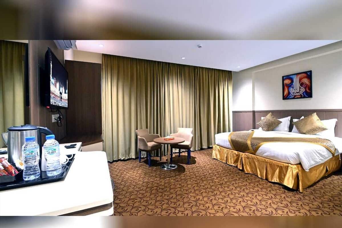 Una camera d'albergo con un letto, una scrivania con una macchina del caffè e bottiglie d'acqua, una sedia e un televisore.