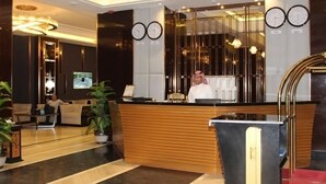 Et hotellets receptionområde med en træreception, to ure på væggen og et tv-skærm over disken.
