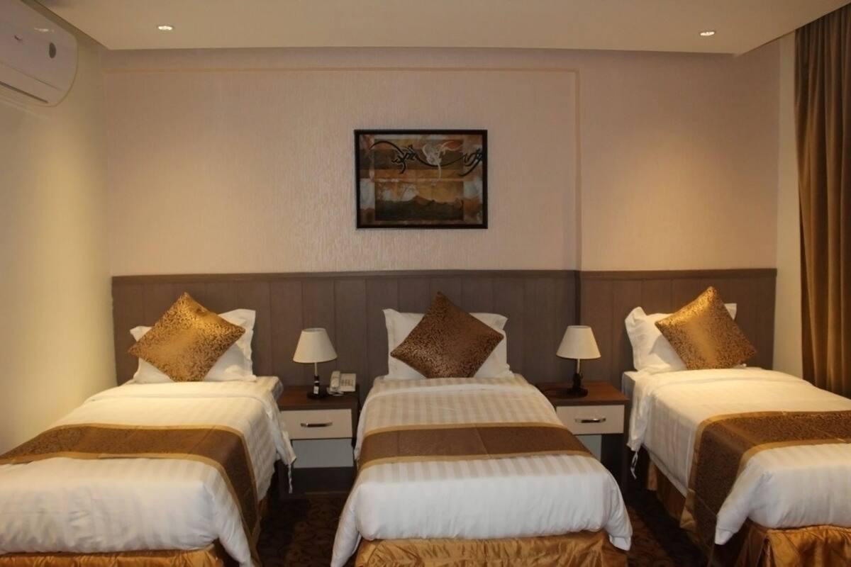 Camera d'albergo con tre letti, ognuno dotato di una testata marrone e biancheria da letto bianca. Sopra i letti, un quadro appeso al muro.