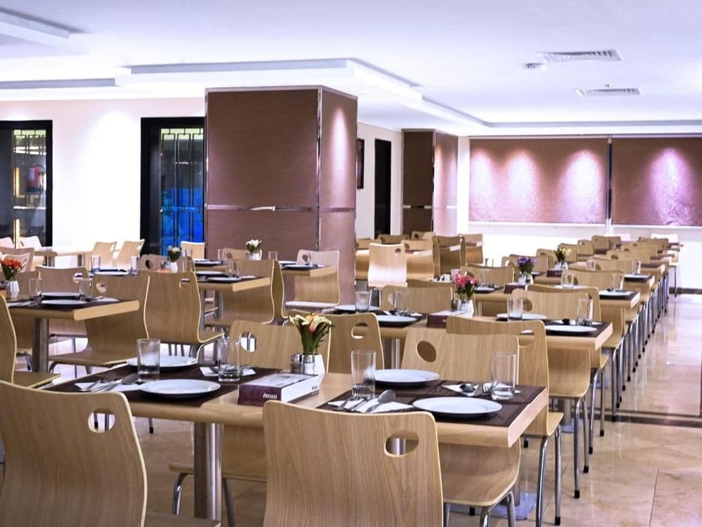 Uma sala de jantar moderna com várias mesas e cadeiras, com louças preparadas e um elemento decorativo central.