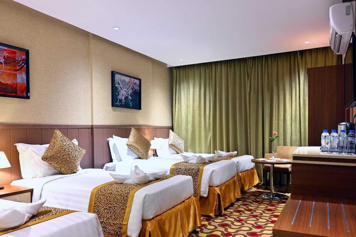 Camera d'albergo con tre letti, una scrivania e un minibar.