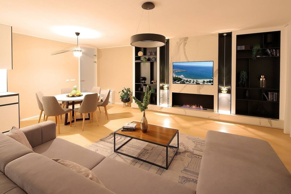 A modern living room with a sofa, coffee table, dining area, and a fireplace with a TV displaying a beach scene.