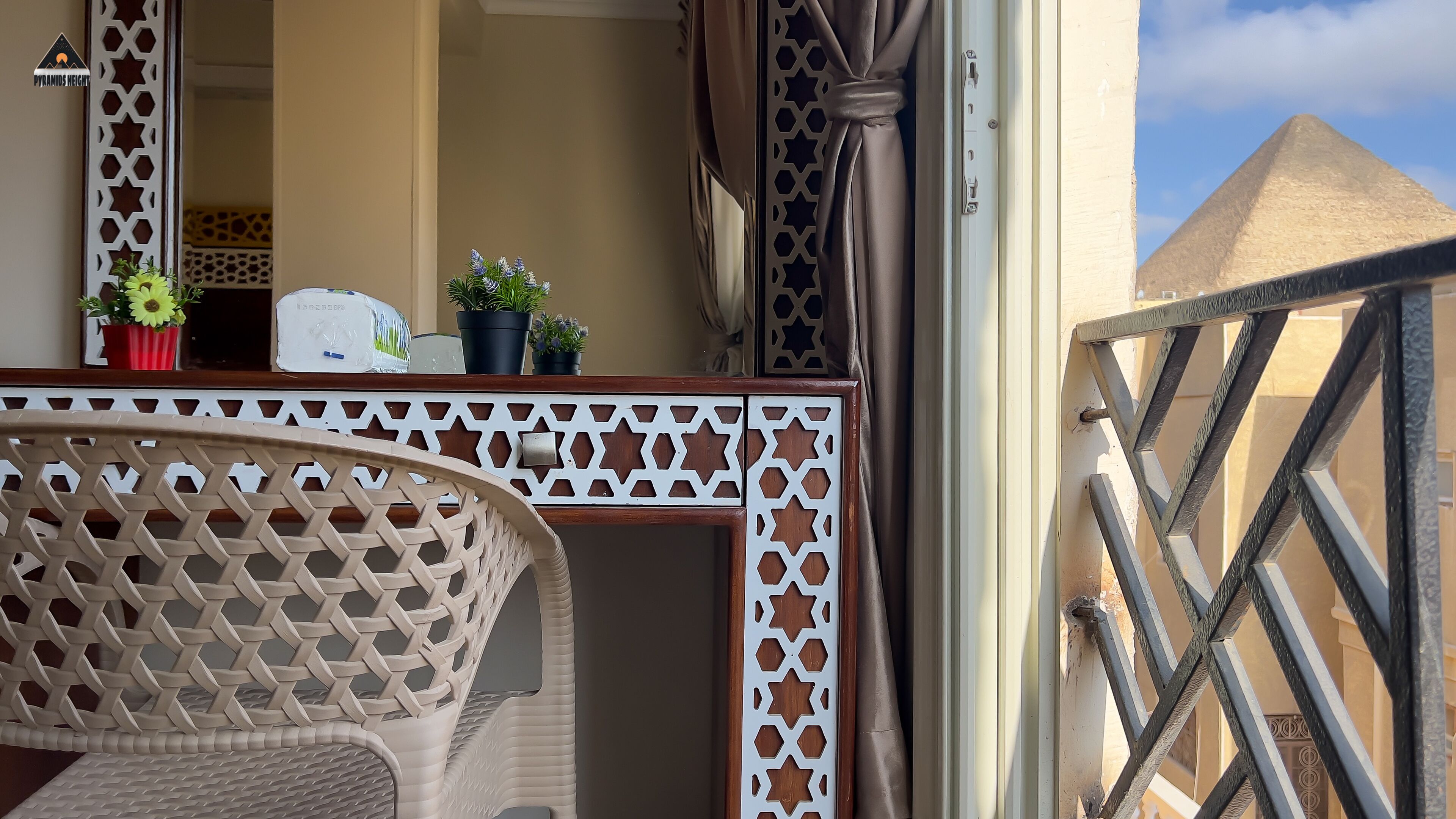 Un balcon agrémenté d’une chaise en osier, d’un pot de fleurs et d’une balustrade blanche décorative en treillis.