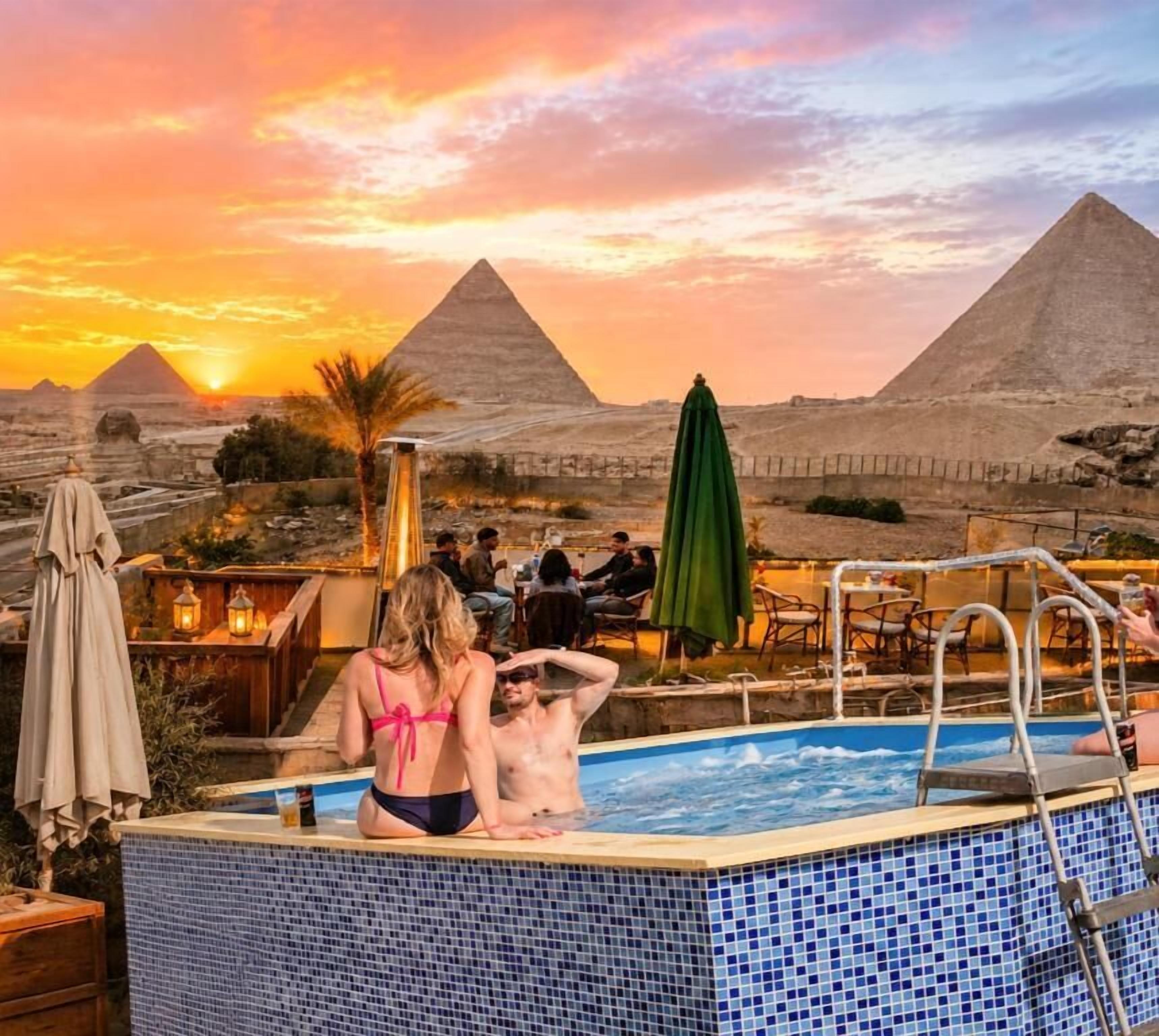 A swimming pool with a view of pyramids at sunset.