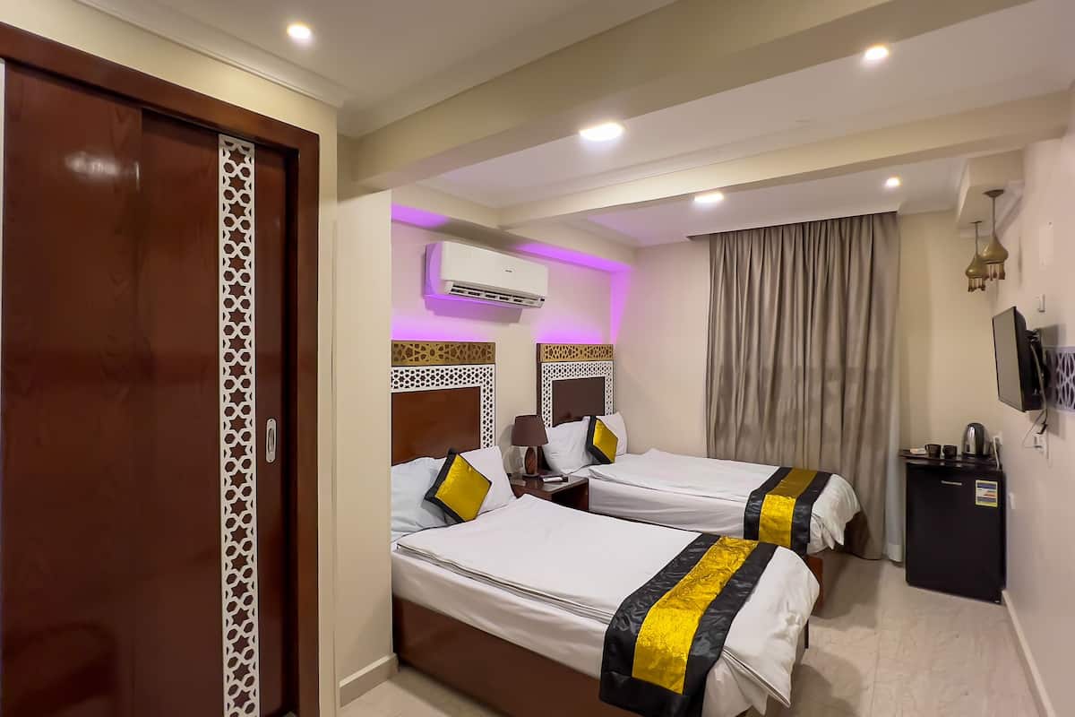 A hotel room with two beds, a TV, an air conditioner, and a curtain.