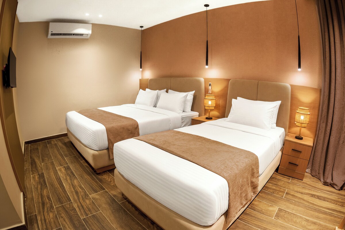 Een hotelkamer met twee bedden, houten vloeren en bedlampjes.