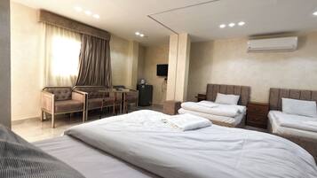 Una habitación de hotel con una cama grande, dos camas más pequeñas, un escritorio y una silla.