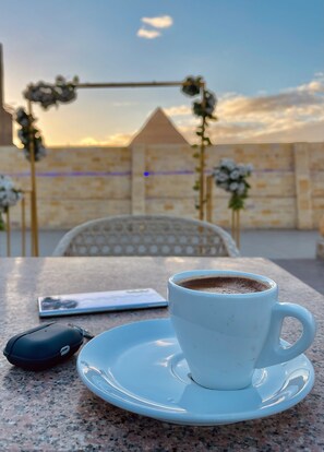 Una taza de café blanca sobre un platillo blanco sobre una mesa de granito. Un teléfono inteligente y un ratón negro están sobre la mesa.