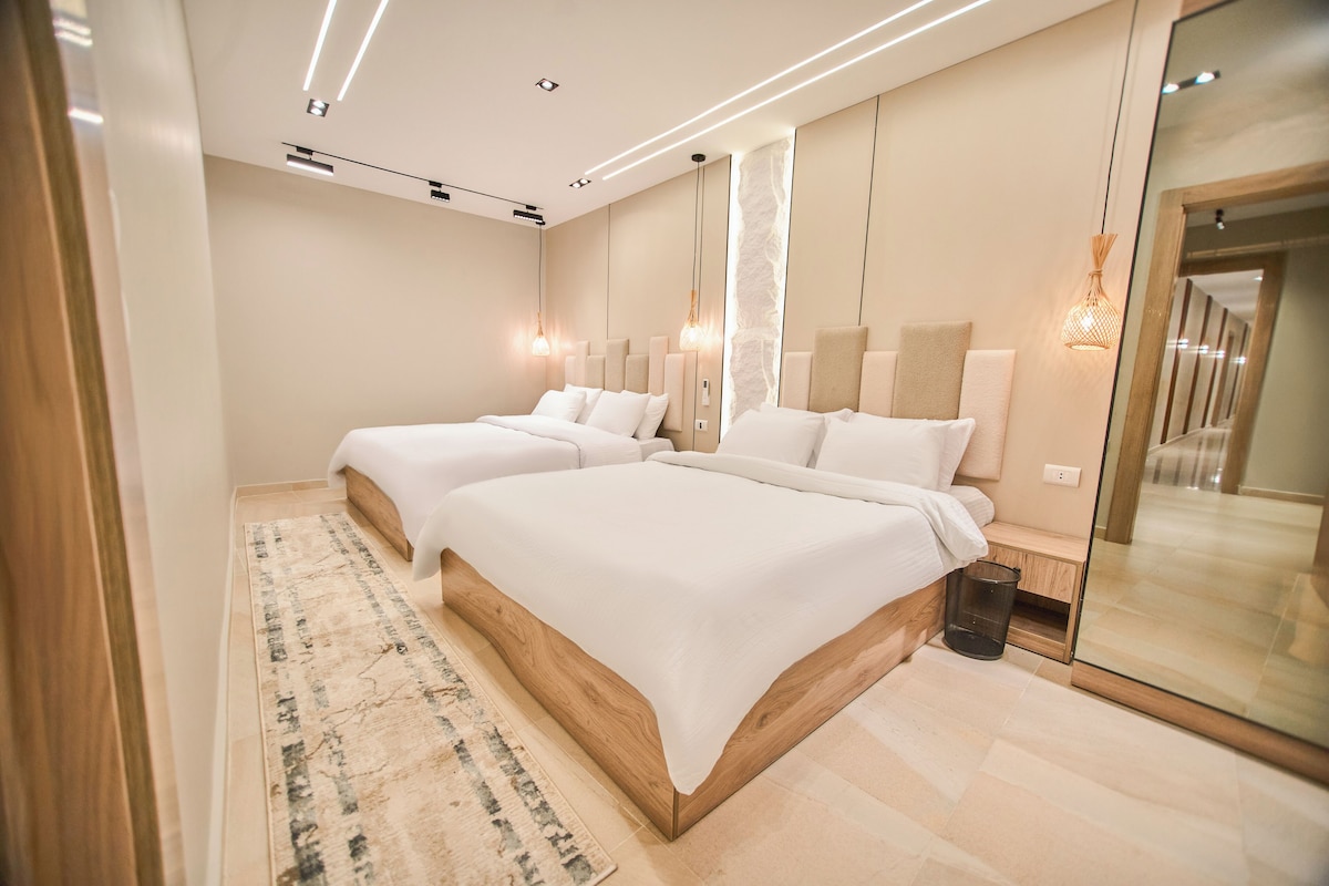 Un dormitorio moderno con dos camas, un espejo grande y una mesita de noche.