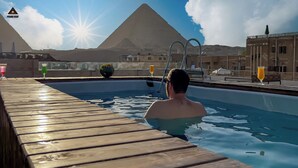Zwembadgedeelte met een houten terras, een persoon in het water en een piramide op de achtergrond.