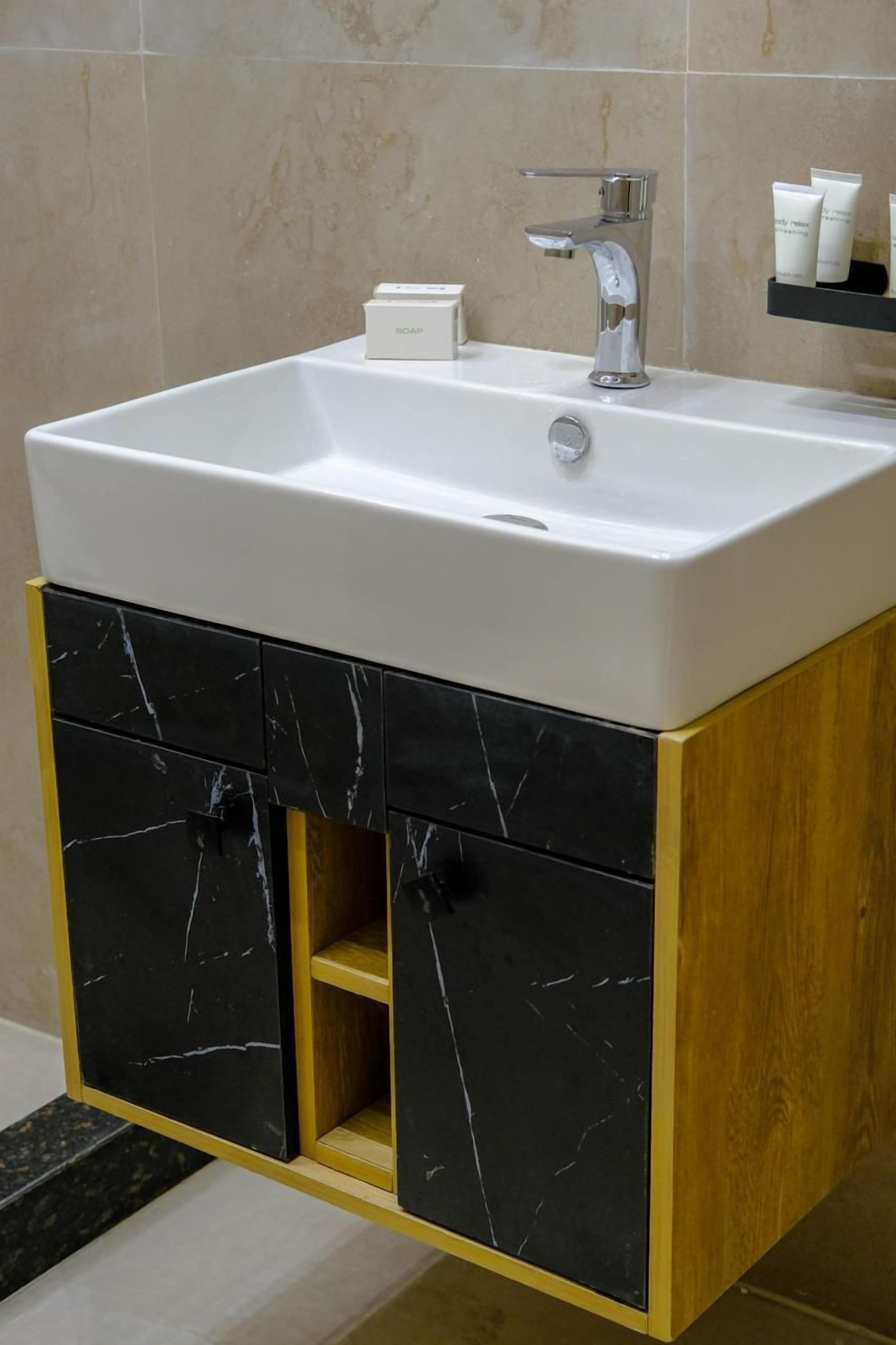 A bathroom with a white sink, black marble cabinets, and a wooden vanity.