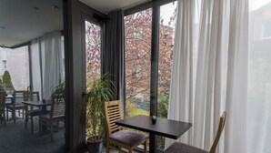 A modern room with a large window, a potted plant, and a table with chairs. - Hotel Jarun (Zagreb)