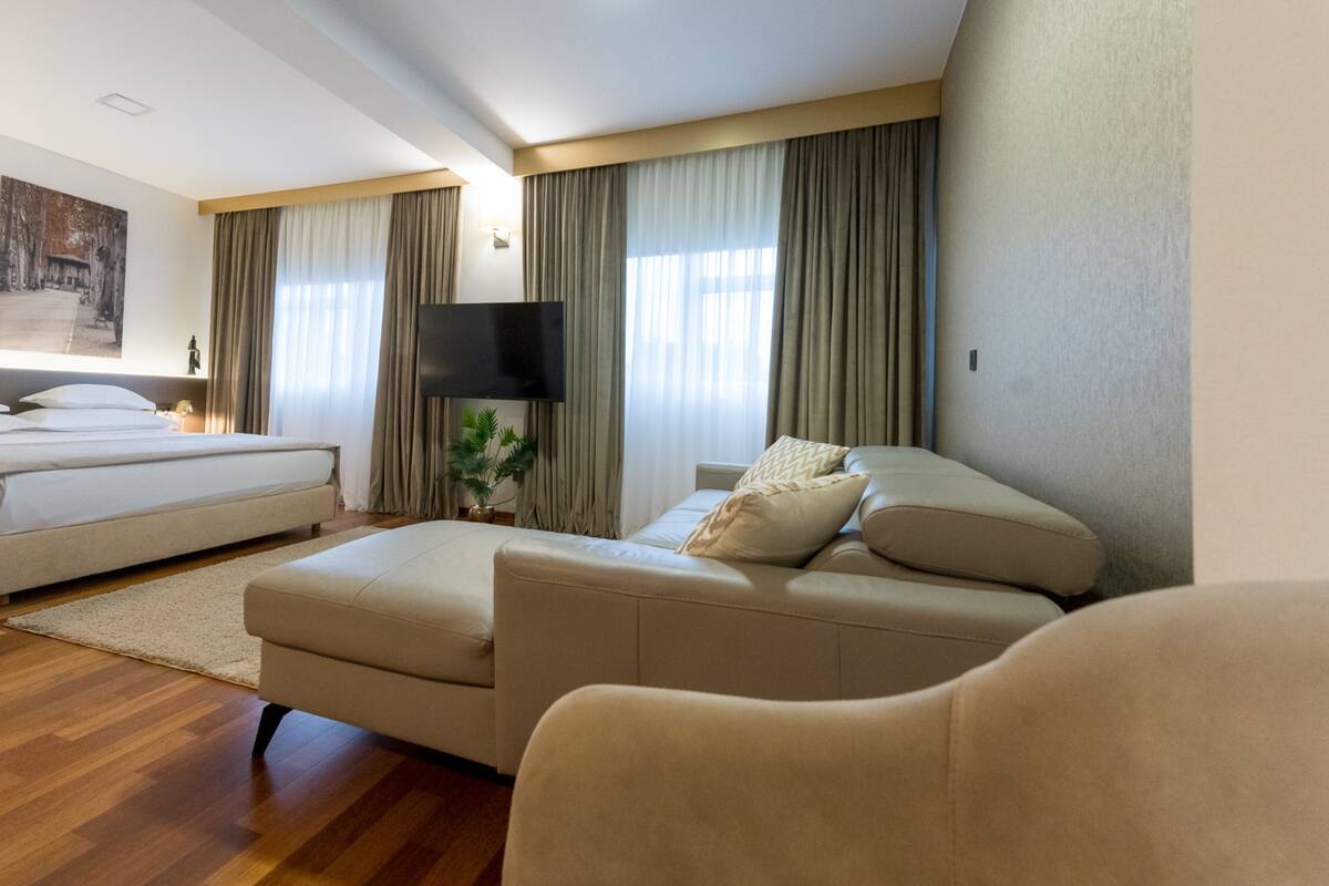 A modern hotel room with a large bed, a sofa, and a flat-screen TV.