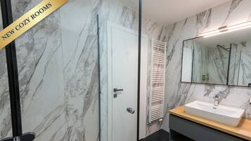 A modern bathroom with a marble wall, a white door, a wooden vanity, and a large mirror.