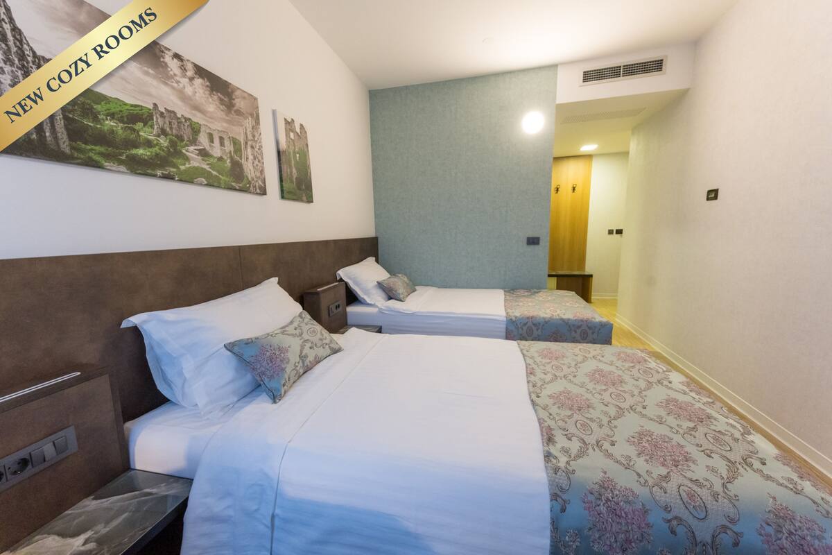 A hotel room with two beds, a nightstand, a small table, and a wall-mounted TV.