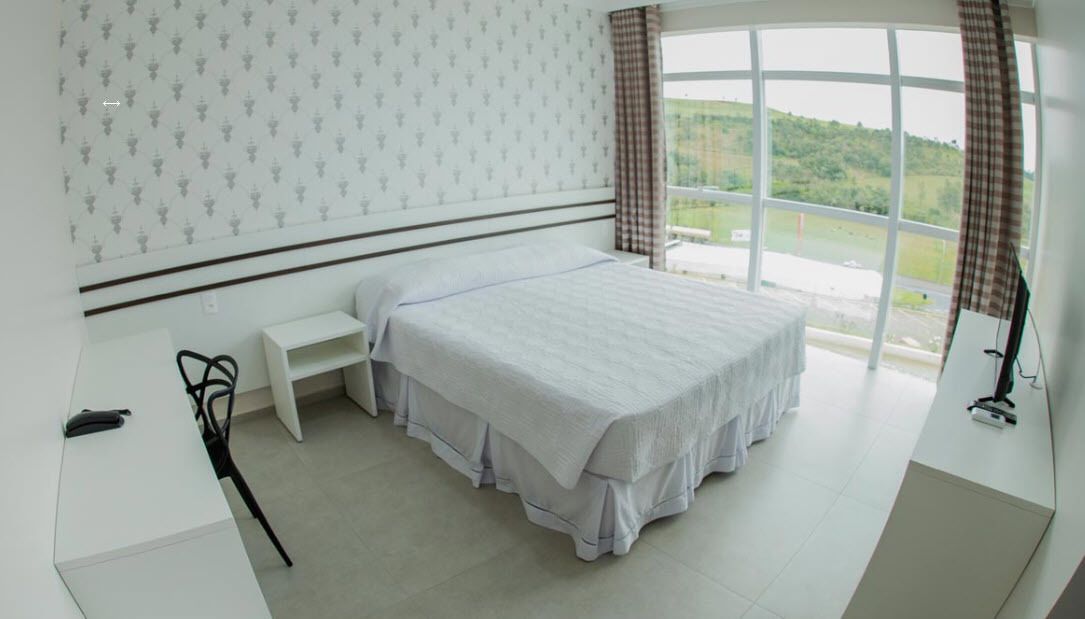 A bedroom with a large bed, a bedside table, a chair, and a window with a view of greenery.