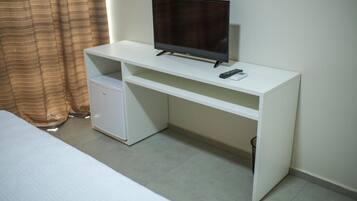 A hotel room with a white desk, a television, a small refrigerator, and a bed.