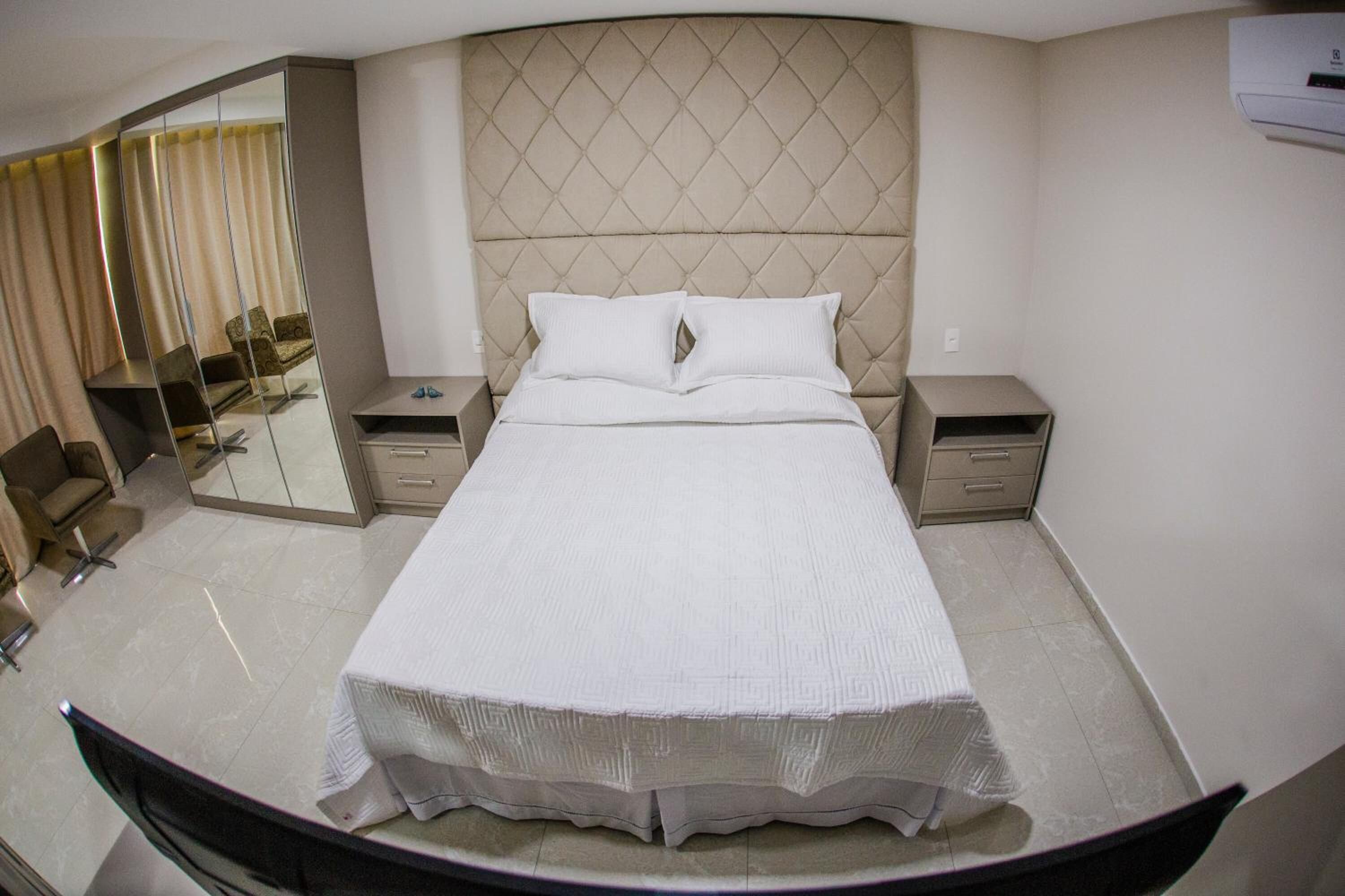 Una habitación de hotel con una cama grande, dos mesitas de noche, un espejo y una silla.