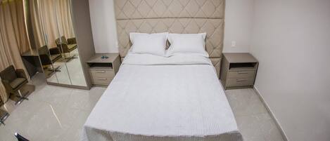 Una habitación de hotel con una cama grande, dos mesitas de noche, un espejo y una silla.