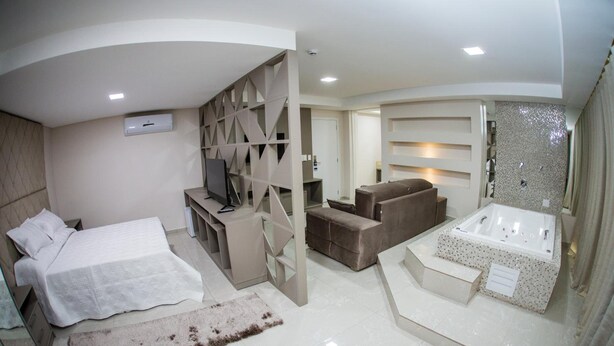A modern hotel room with a bed, a seating area, a TV, and a spa tub. - Hotel HPR Executive (Vitorino)