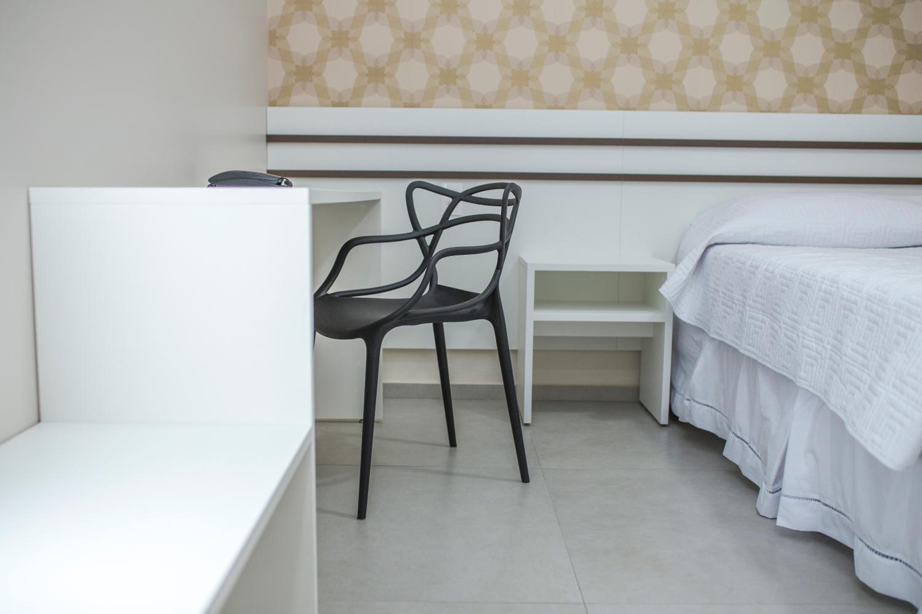 Een slaapkamer met een wit bed, een zwarte stoel en een wit bureau.