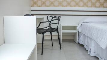 Een slaapkamer met een wit bed, een zwarte stoel en een wit bureau.
