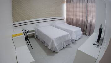 A hotel room with two single beds, a desk, a chair, a TV, and a window with curtains.