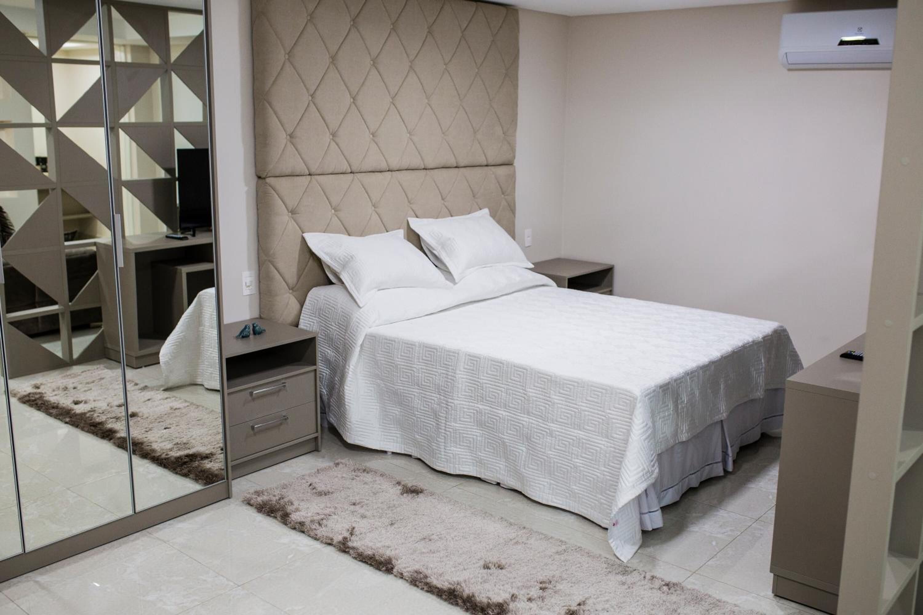 Une chambre à coucher comprenant un lit, des tables de chevet, une armoire et un miroir.