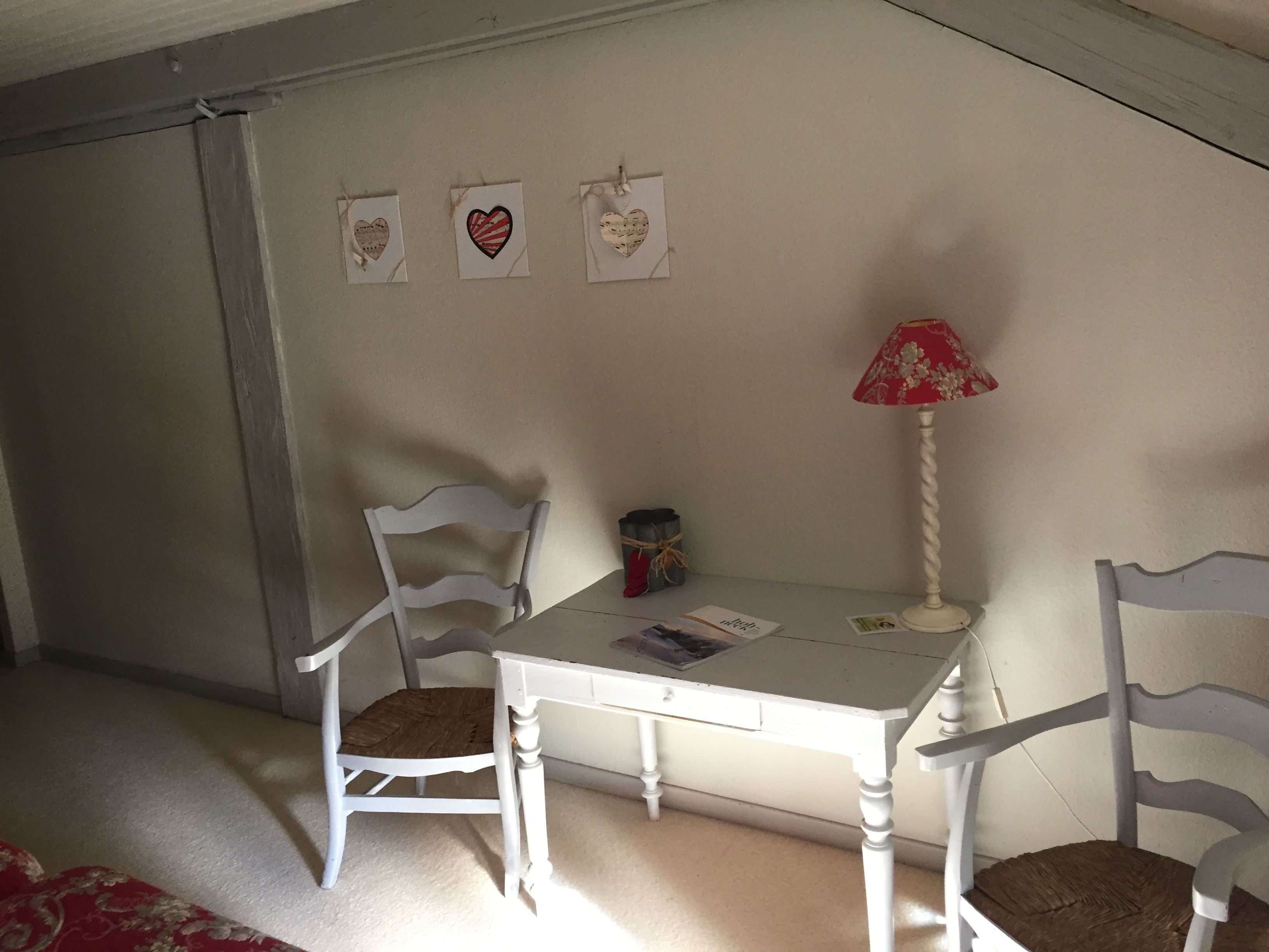 Ein kleiner, gemütlicher Raum mit einem weißen Tisch und zwei weißen Stühlen. An der Wand befinden sich drei herzförmige Verzierungen.