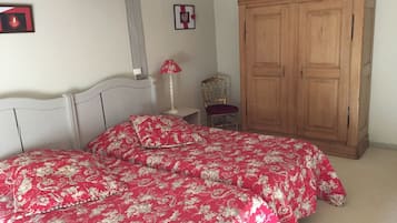 A bedroom with two beds, a wooden wardrobe, a chair, and a bedside table with a lamp.