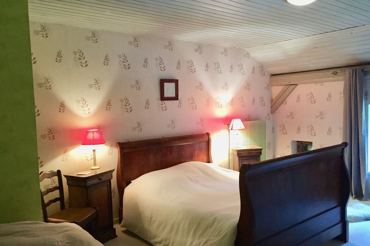 A hotel room with two beds, a wooden headboard, a small bedside table, a chair, and a lamp.