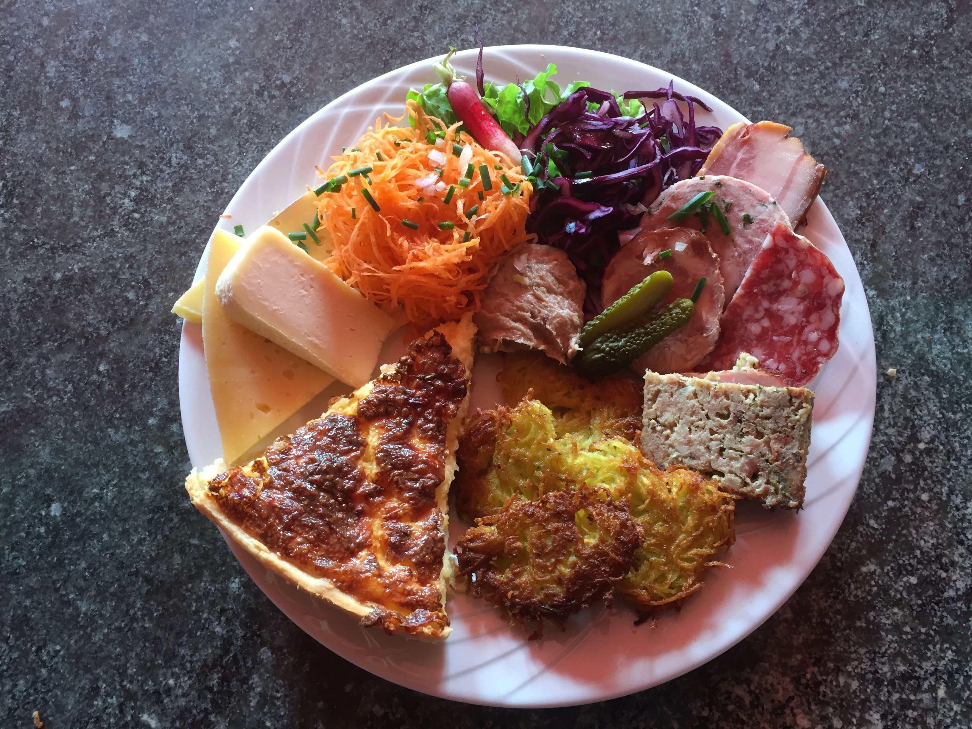 Um prato com vários alimentos, incluindo uma fatia de torta, um pedaço de carne e uma salada.