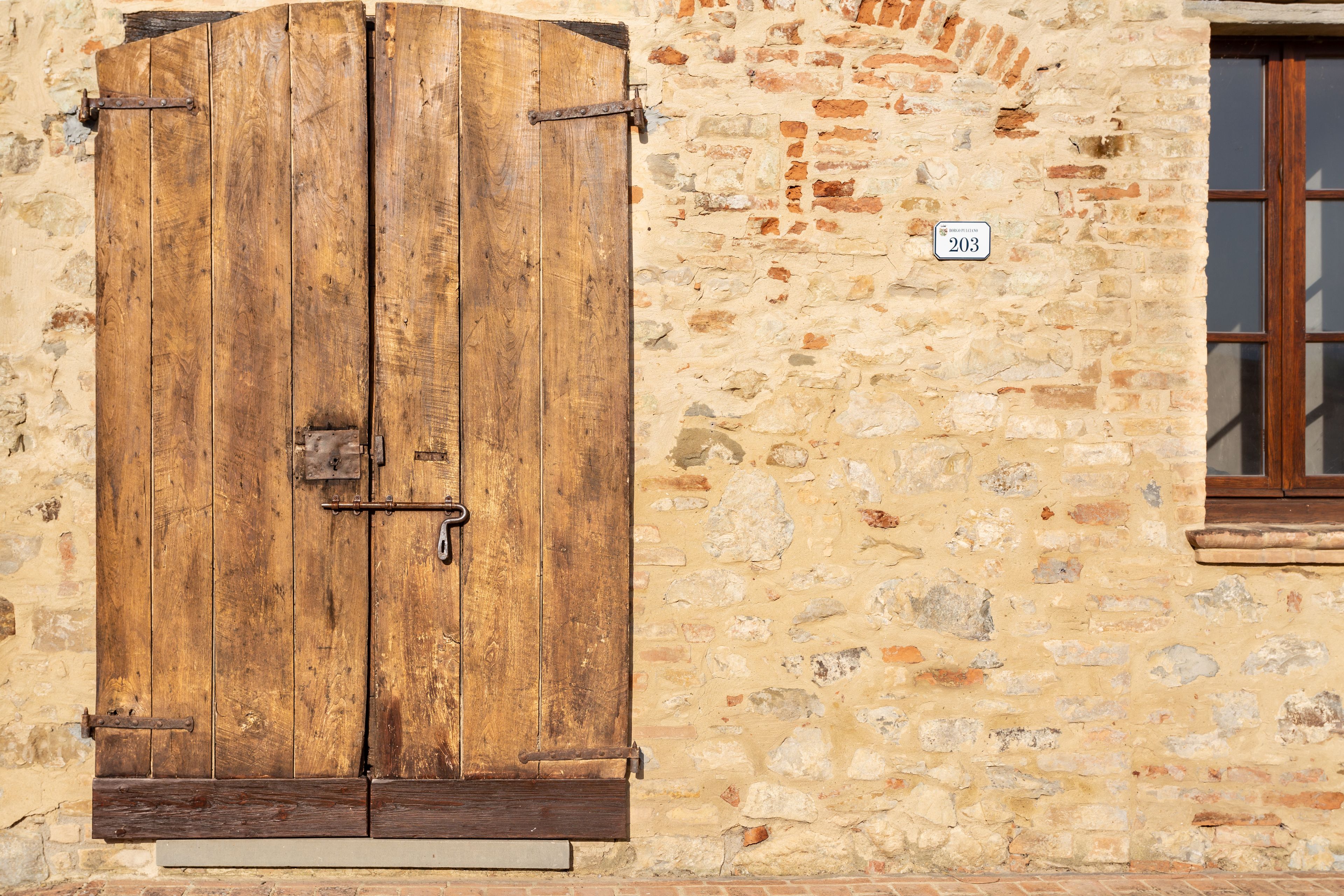 A rustic stone building with a large wooden double door and a small window with a wooden frame.