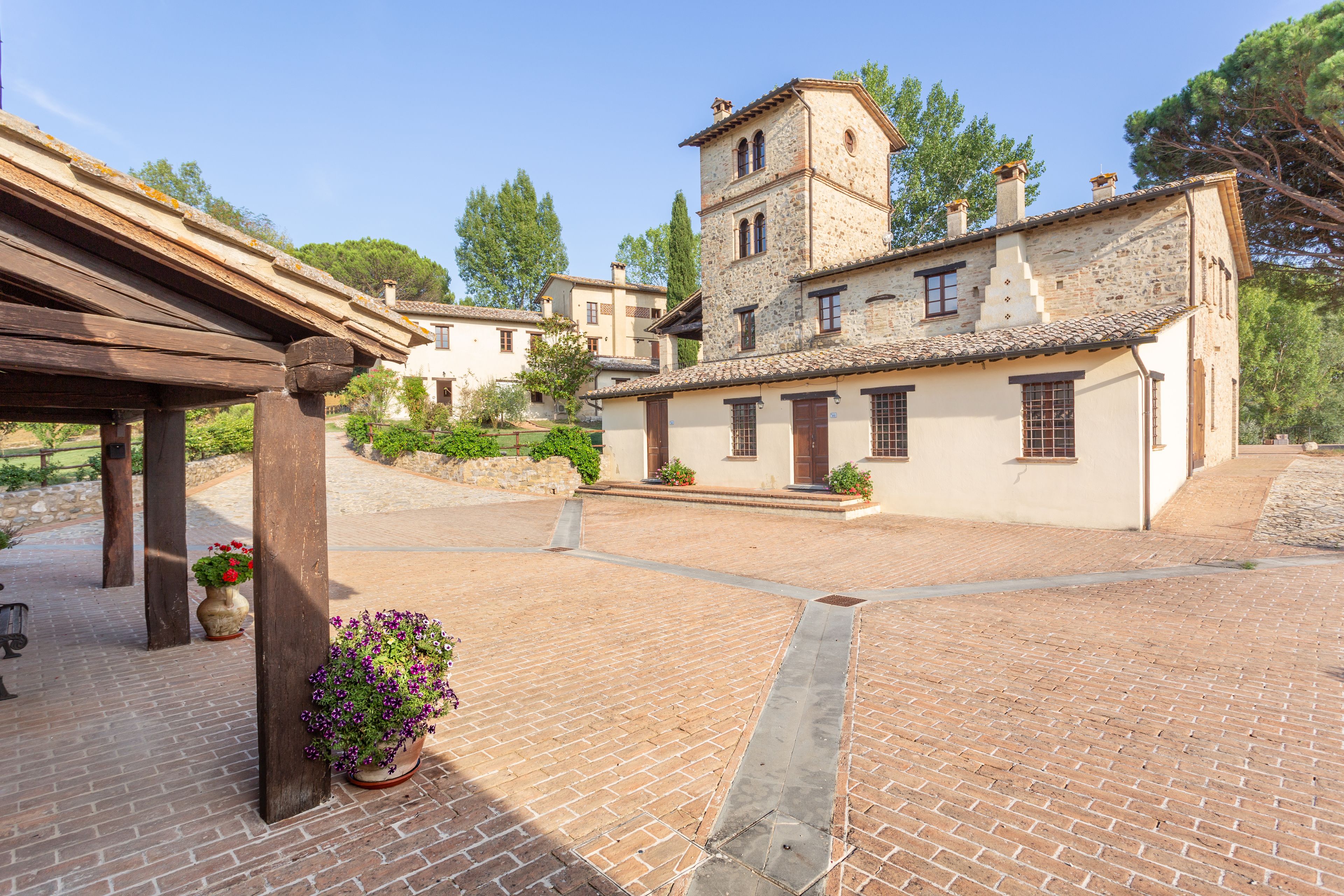 Un patio con un edificio de piedra, una pérgola de madera y plantas en macetas.
