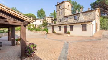 Un patio con un edificio de piedra, una pérgola de madera y plantas en macetas.