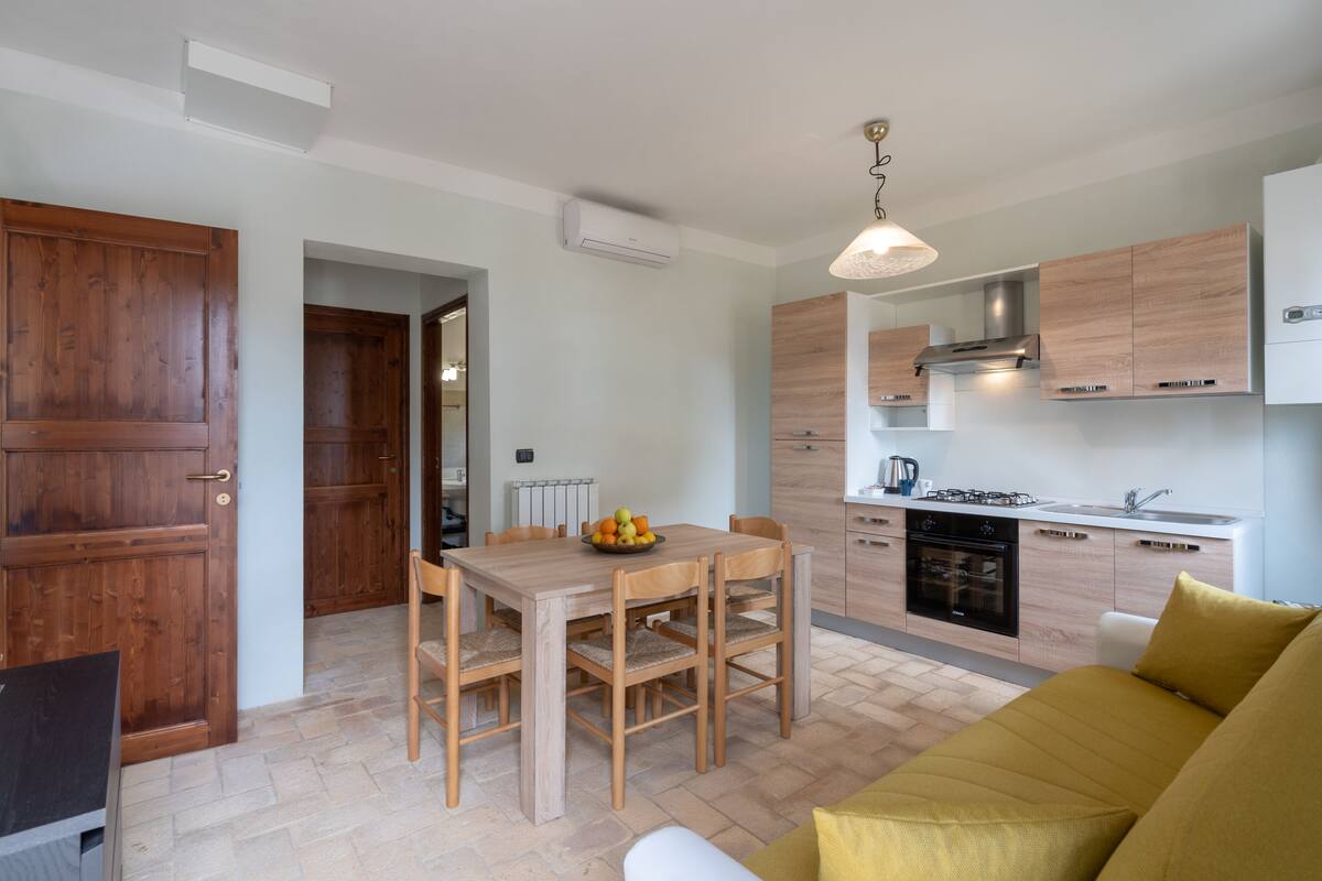 Een moderne keuken met houten kastjes, een eettafel met stoelen en een geel bankje.