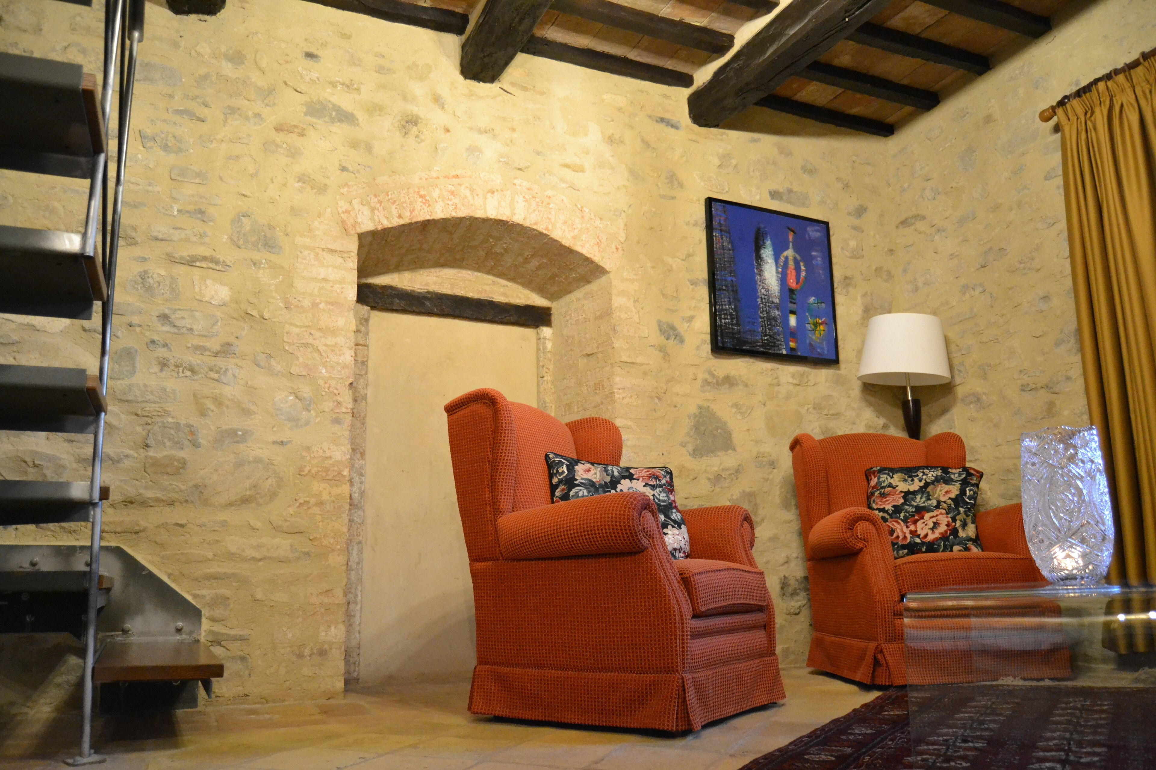 A cozy room with two orange armchairs, a wooden staircase, and a stone wall.