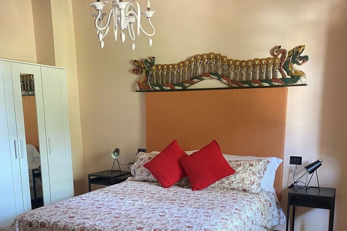 Een slaapkamer met een bed, nachtkastje, lamp, kledingkast en een decoratief hoofdeinde.