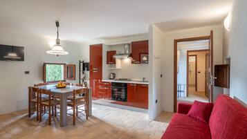 A modern kitchen with red cabinets, a dining area with wooden chairs, and a red sofa in a living room.