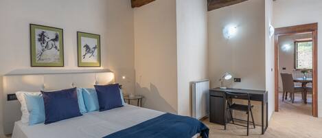 Un dormitorio con cama, mesitas de noche, un escritorio y una silla. Hay dos cuadros en la pared.