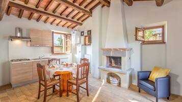 A cozy kitchen with wooden beams, a dining table with chairs, a fireplace, and a blue sofa with a yellow pillow.