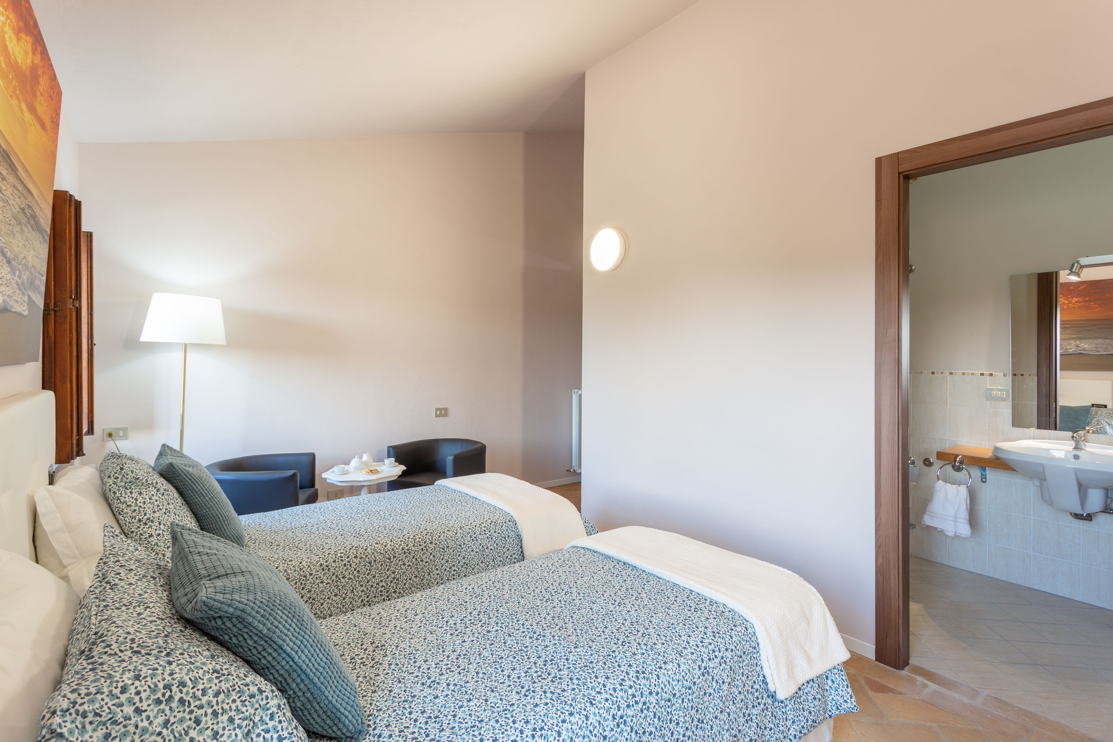Hotelkamer met twee bedden, een bureau, een stoel, een lamp en een zichtbare badkamer door een geopende deur.