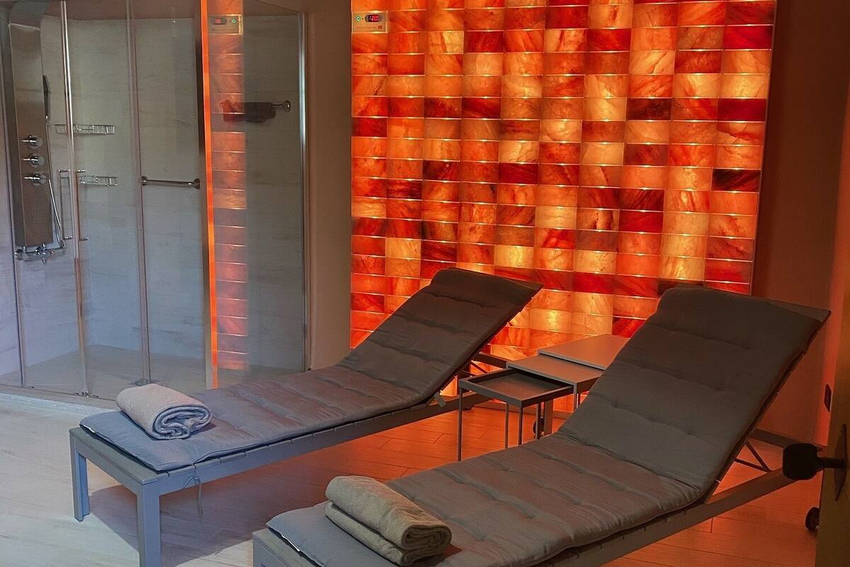 Een wellnessruimte met twee comfortabele stoelen, een glazen douchecabine en een muur met een warme, gloeiende decoratie.