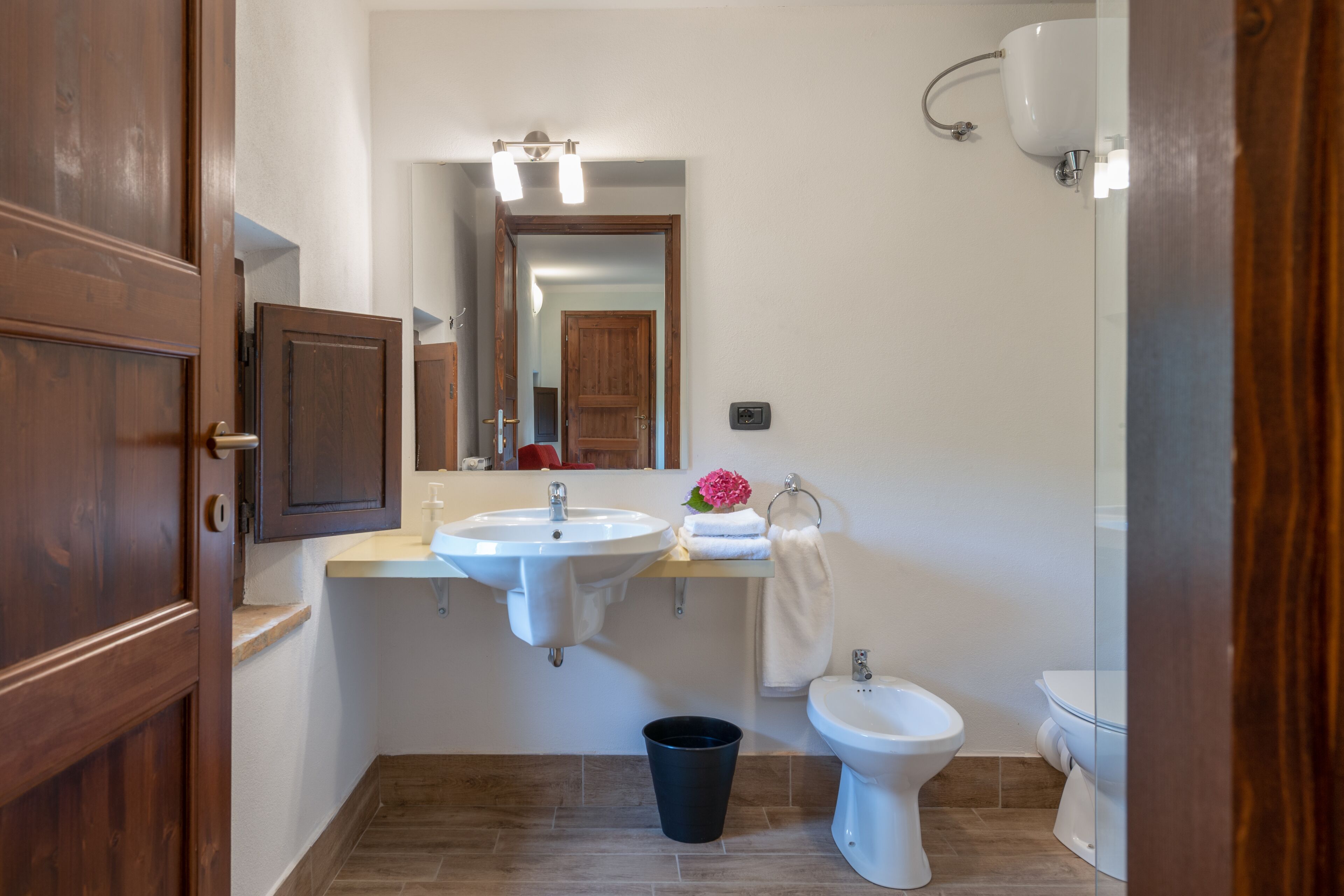 A modern bathroom with a wooden door, a sink, a bidet, and a toilet.